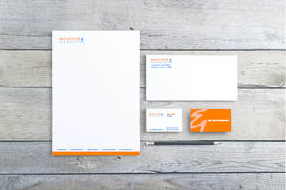 Image of letterhead, envelope and business cards with a Moulton & Associates logo in orange laying on a gray wood background.